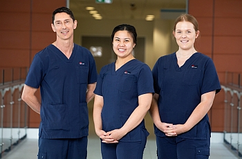 Three smiling clincians standing next to each other in their blue uniform